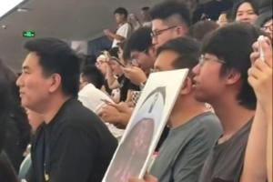 詹姆斯中国行成都活动现场 一球迷拿着詹姆斯经典哭脸照坐在场边